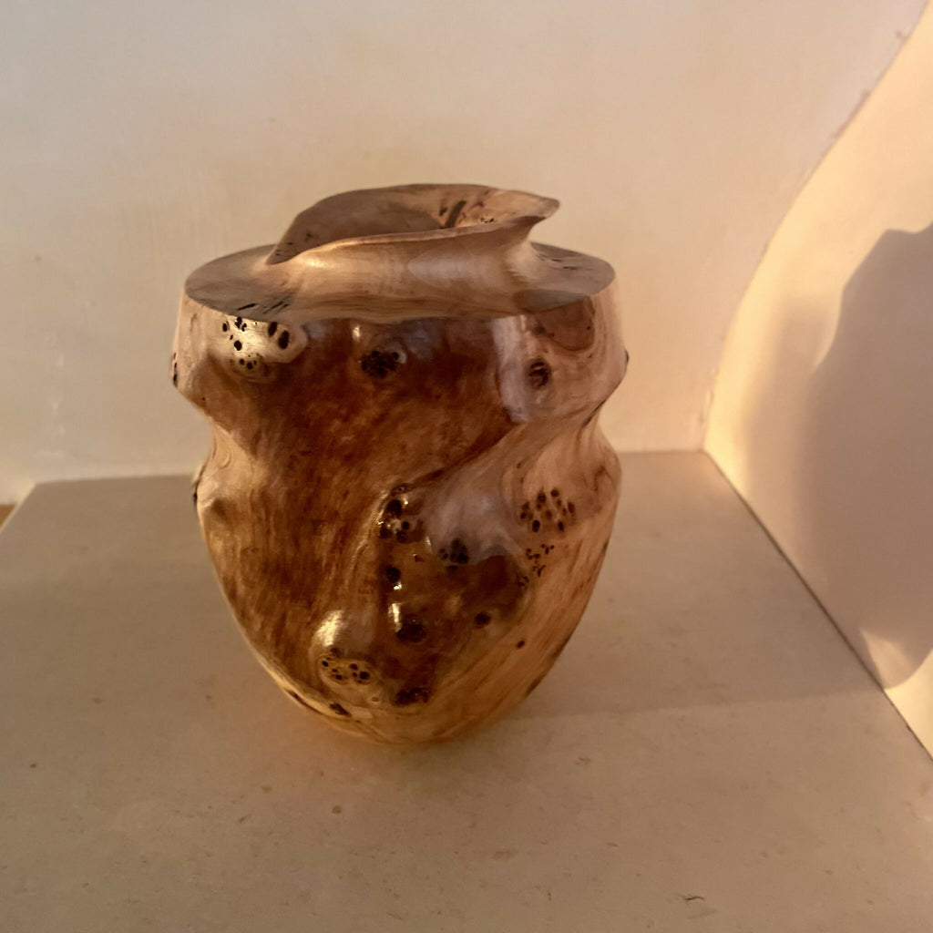 Vase en bois sculpté couleur miel, vue de côté, ouverture sobre et taches sombres.