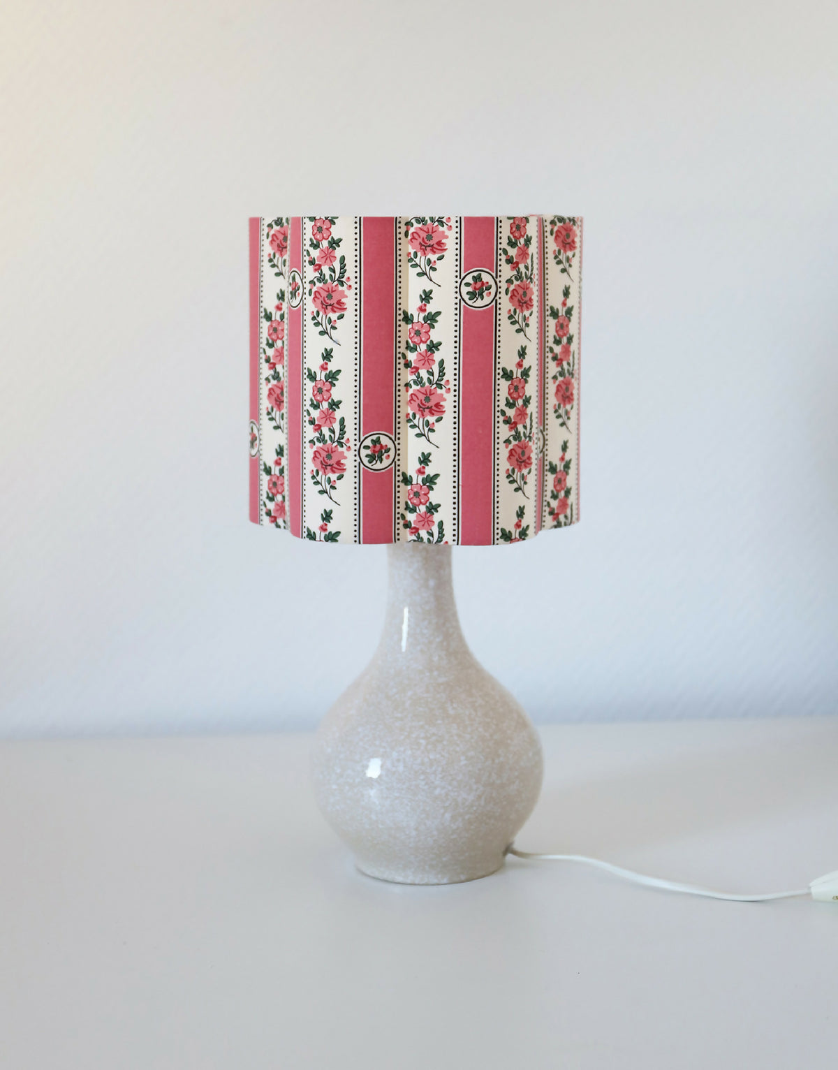 Abat-jour forme fleur à rayures roses et fleurs, posé sur pied de lampe.