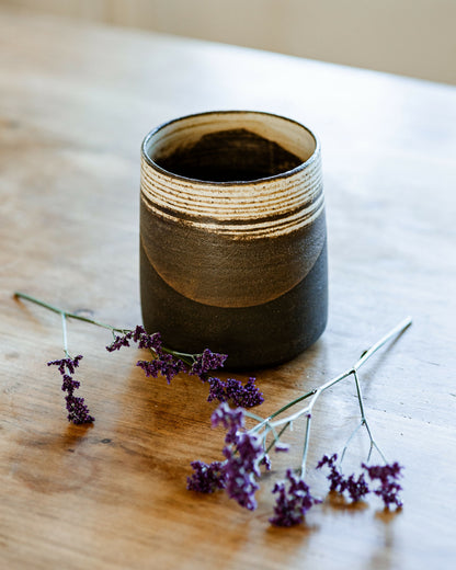 Vase en céramique à rayures dorées et base sombre sur table en bois