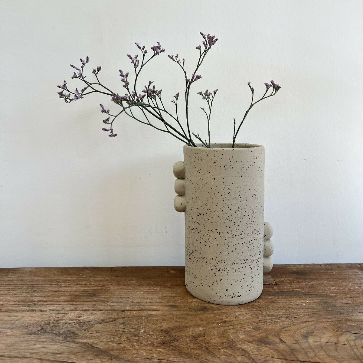 Vase en grès beige piqueté avec reliefs ronds sur le côté, silhouette cylindrique.