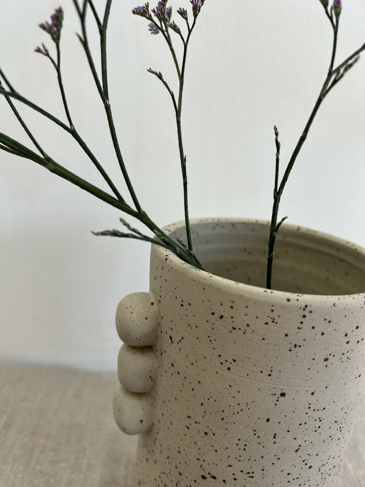 Vase en grès beige piqueté, gros plan sur les reliefs ronds et l’ouverture évasée.