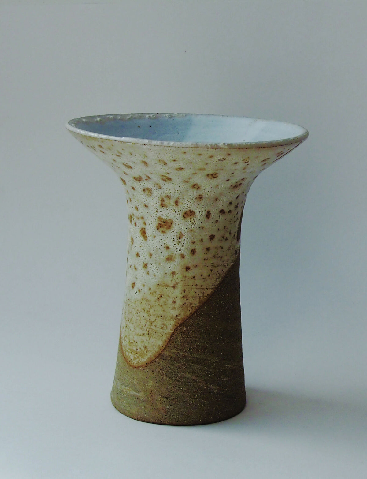 Vase tulipe en céramique beige et vert, bord intérieur bleu, surface tachetée.