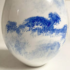 Vase blanc avec motif bleu de paysage et végétation, touches aquarelle.
