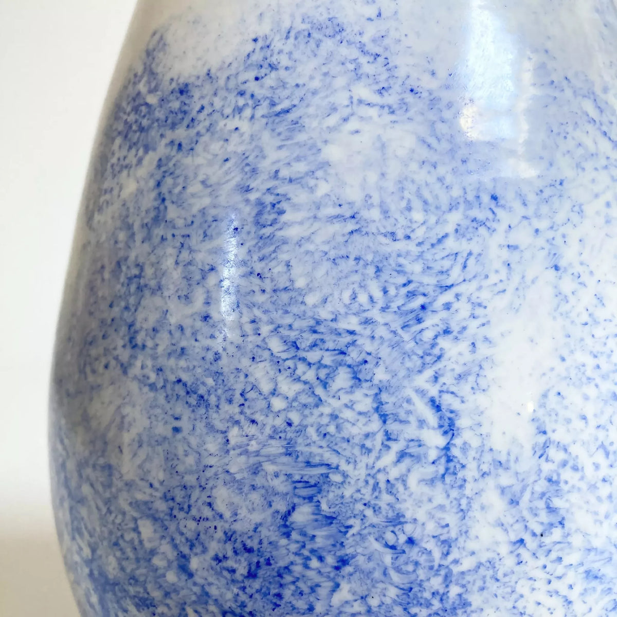 Vase goutte, gros plan motifs bleus et traînées sur surface blanche brillante.