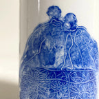 Vase blanc, gros plan sur couple méditant en bleu et motifs de lignes.