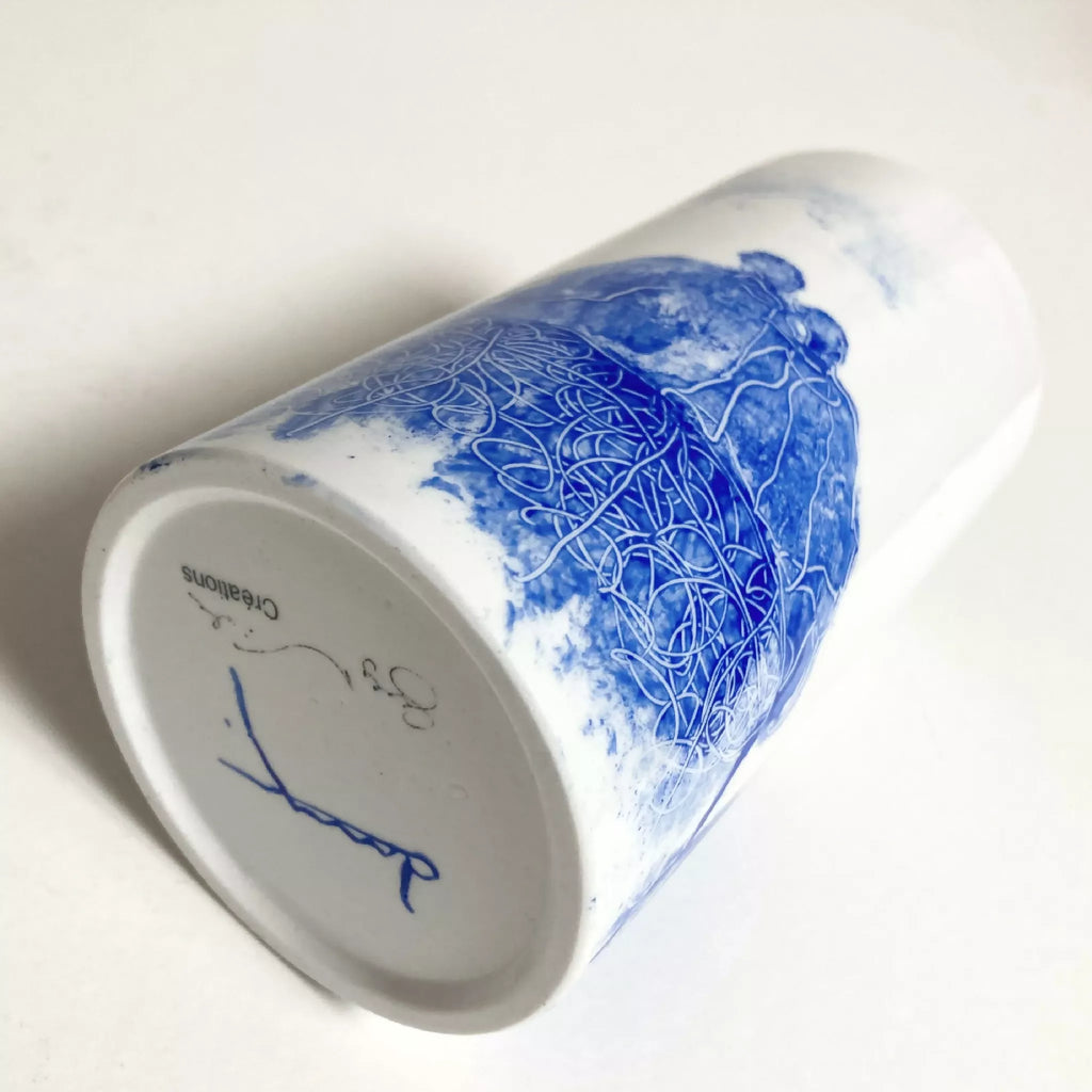 Vase cylindrique blanc, vue du dessous avec marque et motif bleu sur l’extérieur.