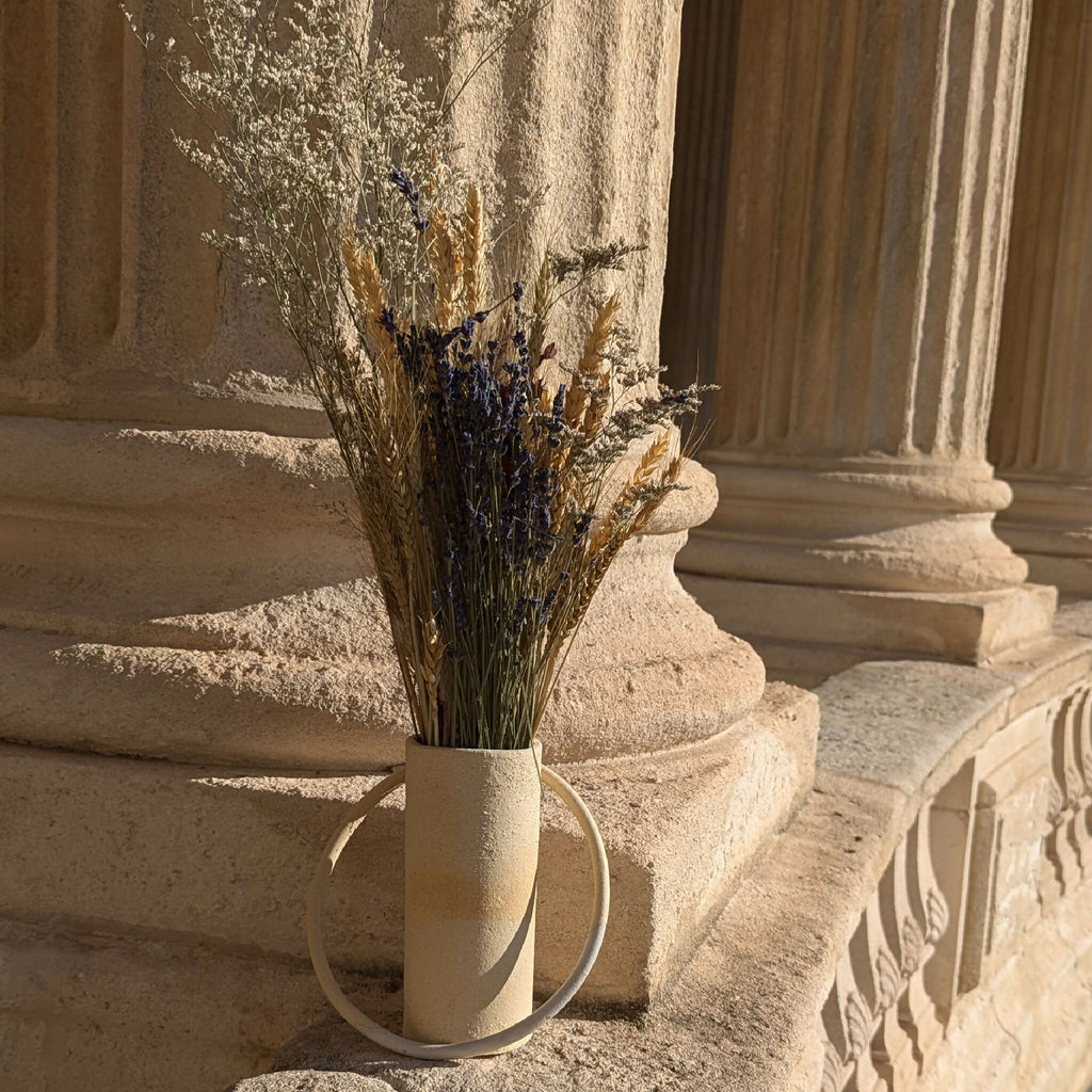 Vase en céramique beige avec anse et fleurs séchées, posé sur un socle.