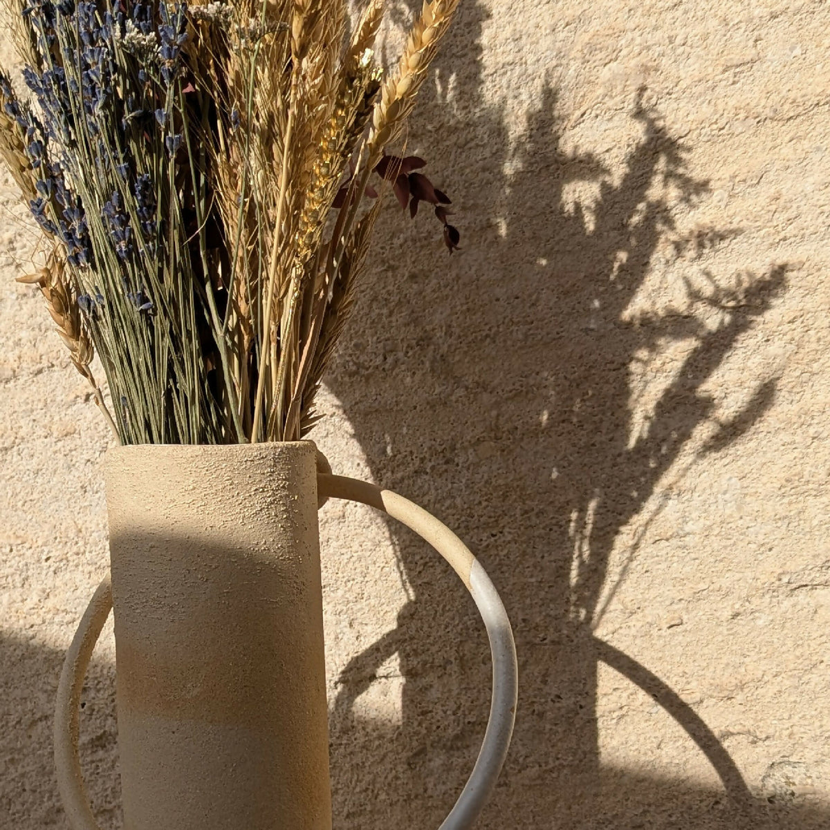 Vase en céramique beige avec anse, fleurs séchées visibles, vue rapprochée.