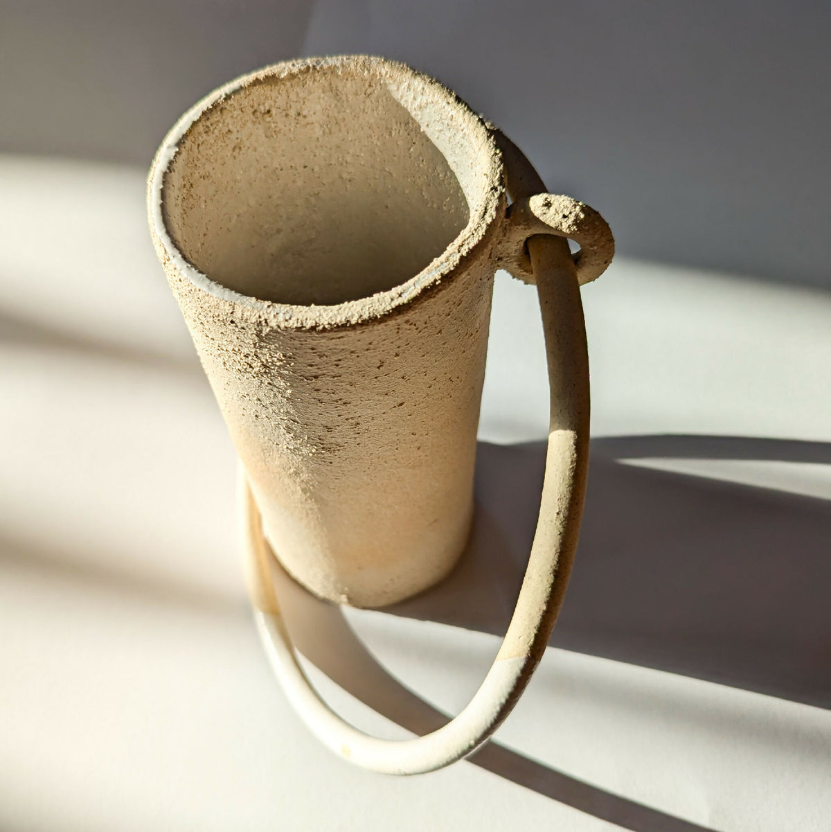 Vase en céramique beige à anse en U, intérieur visible, surface texturée.