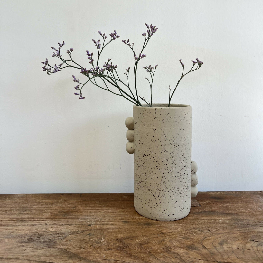 Vase en grès beige piqueté avec reliefs ronds sur le côté, silhouette cylindrique.