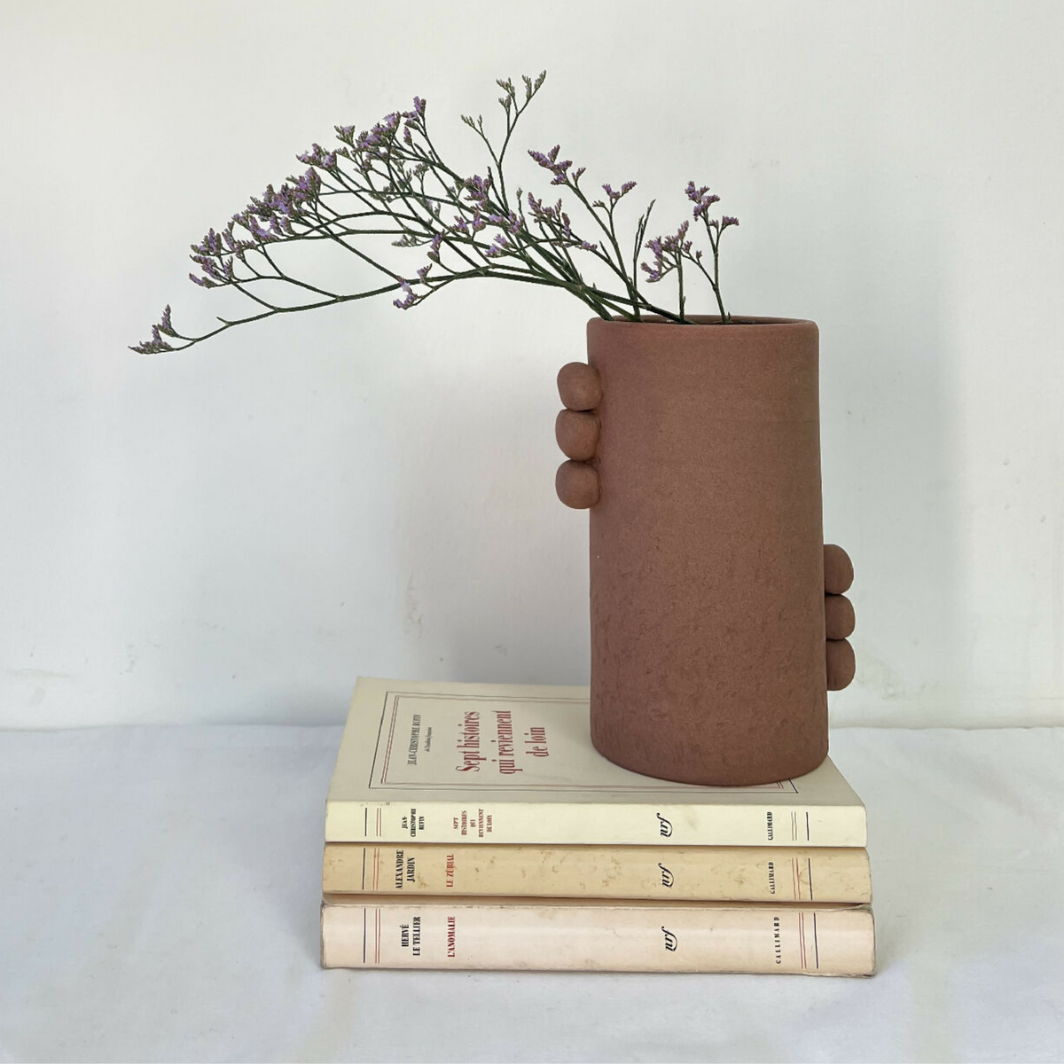 Vase en grès brun cylindrique, bouquet violet et pile de livres, vue d’ensemble.