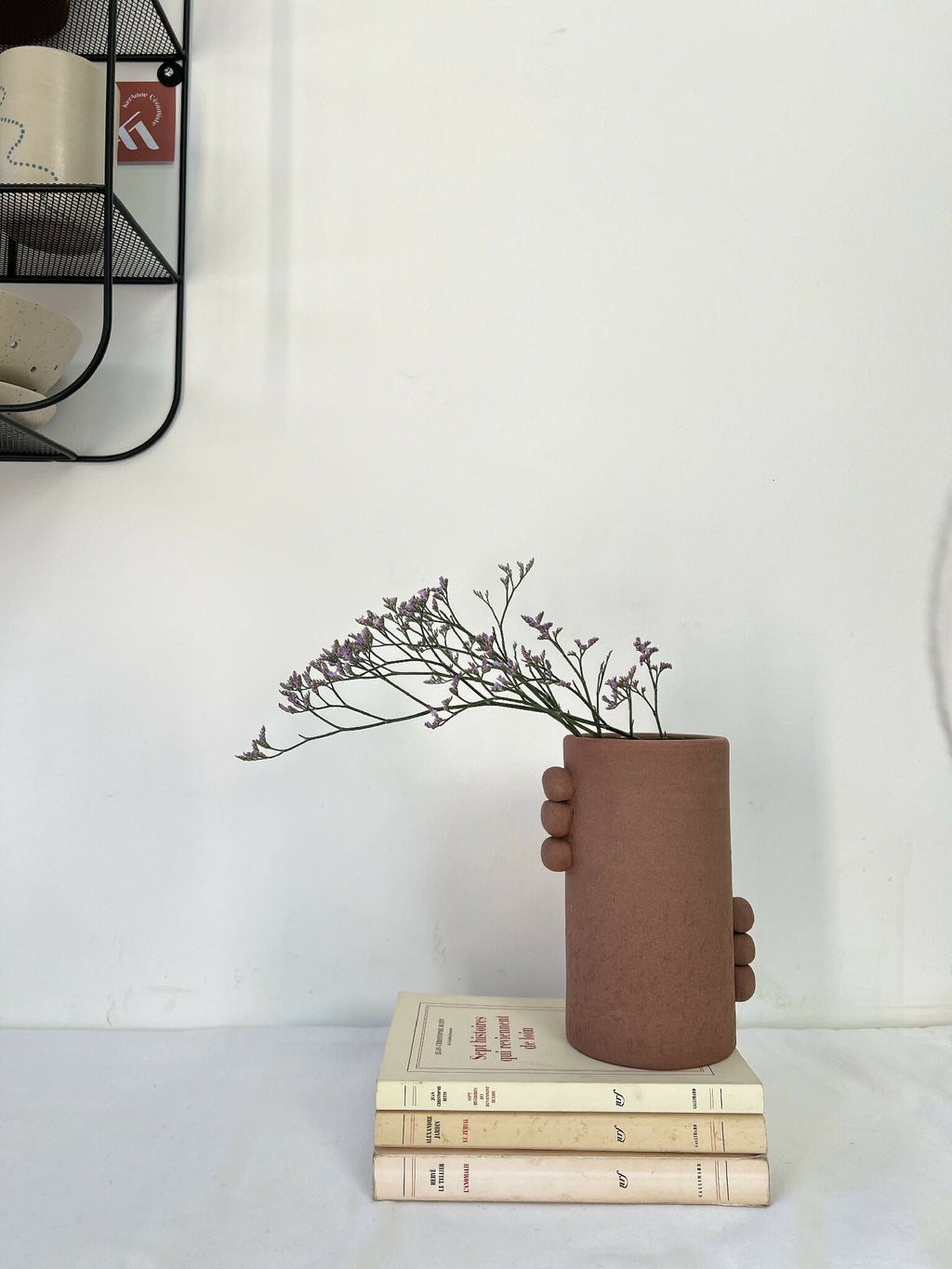Vase en grès brun avec bouquet violet, sur une pile de livres, vue de face.