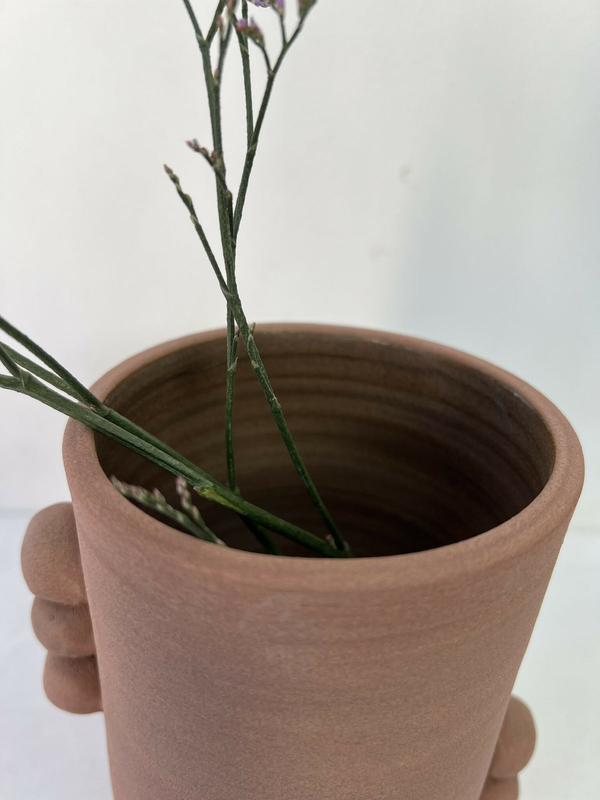 Vase en grès brun, vue intérieure avec tiges de fleurs vertes et bouquet.