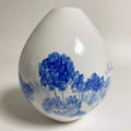 Vase en céramique goutte blanche avec paysage bleu et arbres.
