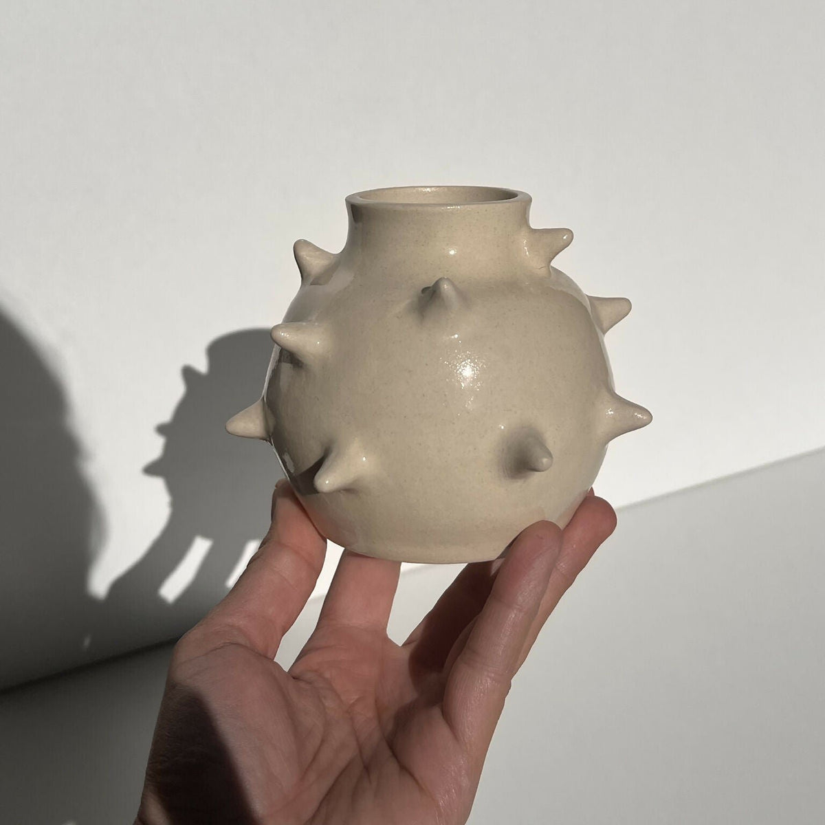 Vase en céramique beige à reliefs pointus, tenu dans la main, ouverture en haut