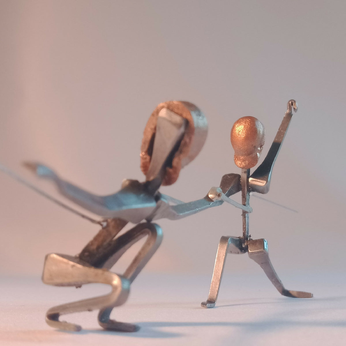 Deux figurines d’escrimeuses en acier, positions opposées, détails bleus et têtes cuivre.