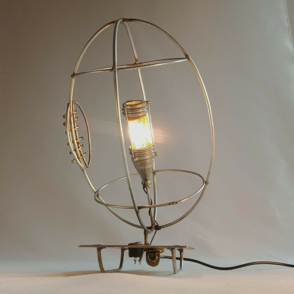Lampe RUGBY allumée avec cage ronde dorée et ampoule à filament, sur pied