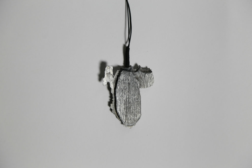 Pendentif gris en forme de feuille d’arbre, vue de profil, sur cordon noir.