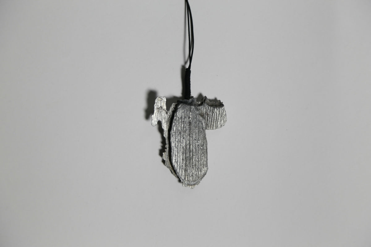 Pendentif gris en forme de feuille d’arbre, vue de profil, sur cordon noir.