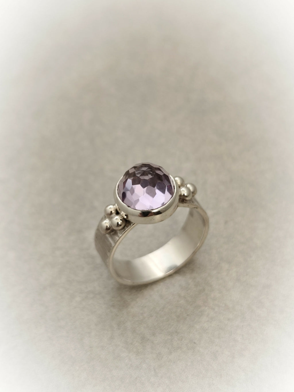 Bague en argent avec pierre améthyste ronde facettée et trois petites perles décoratives.