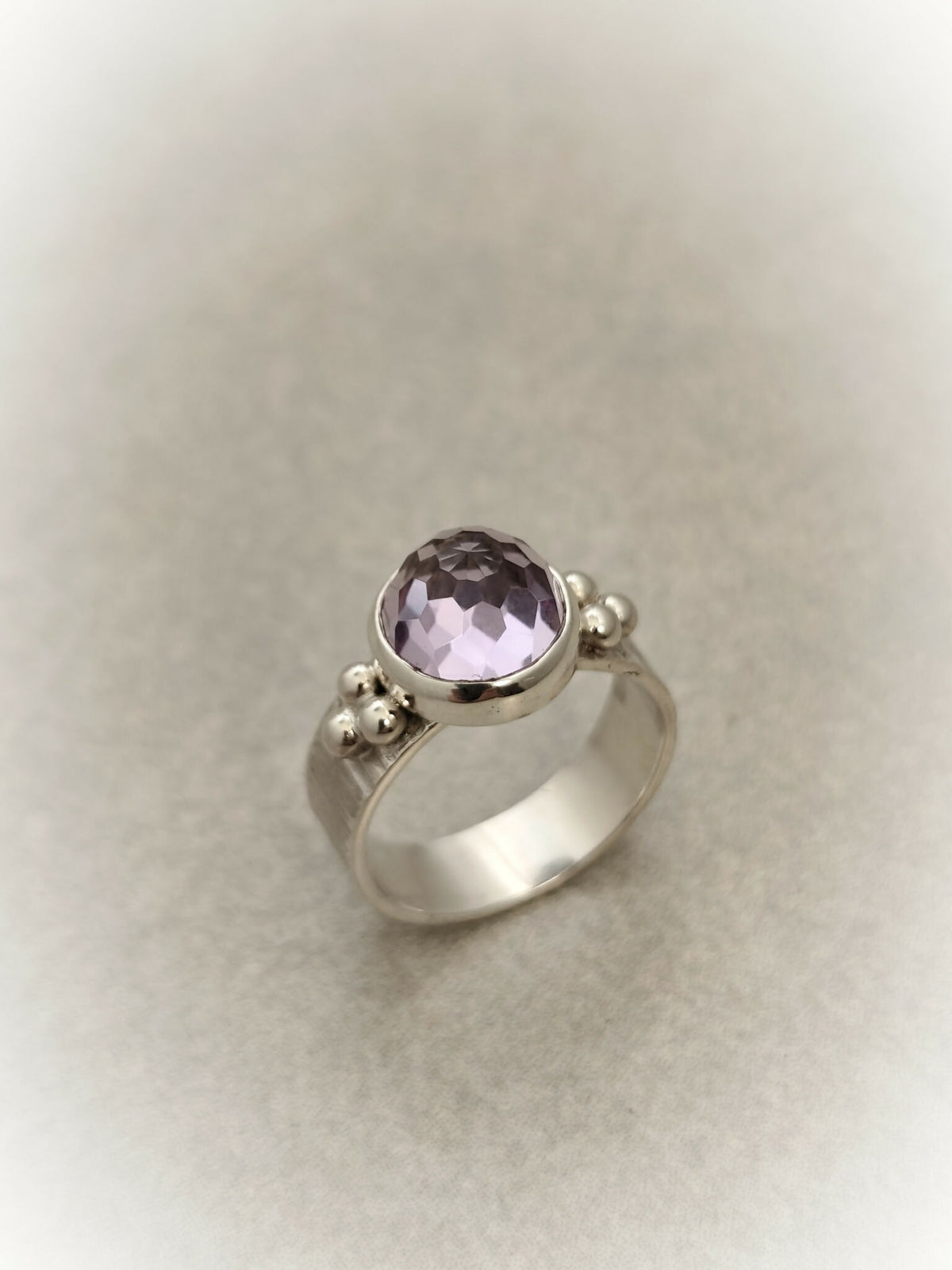 Bague en argent avec pierre améthyste ronde facettée et trois petites perles décoratives.