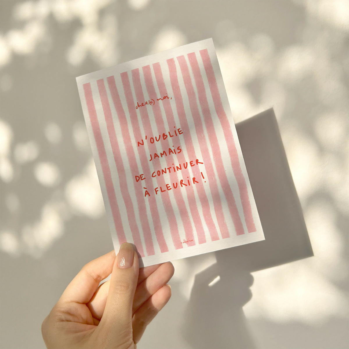 Carte de vœux rayée rose tenue en main, message « N’oublie jamais… à fleurir ! »