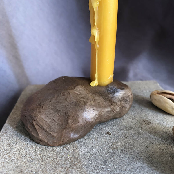 Mini bougeoir en pierre brune avec bougie jaune allumée, tige centrale.
