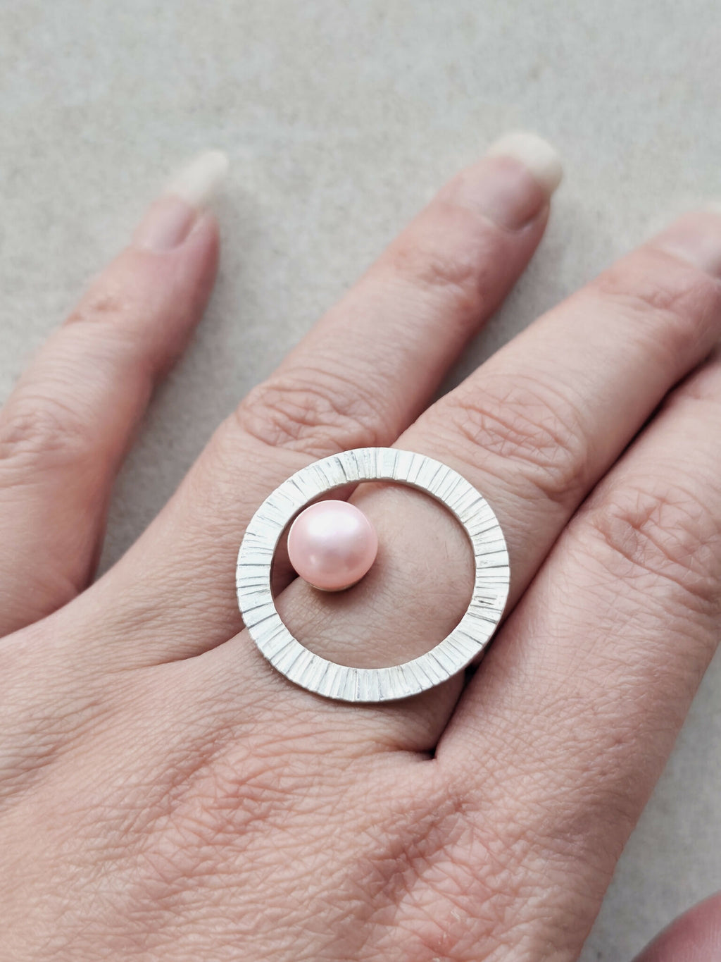 Bague Atoll argentée avec cabochon perle rose et anneau strié, portée sur la main