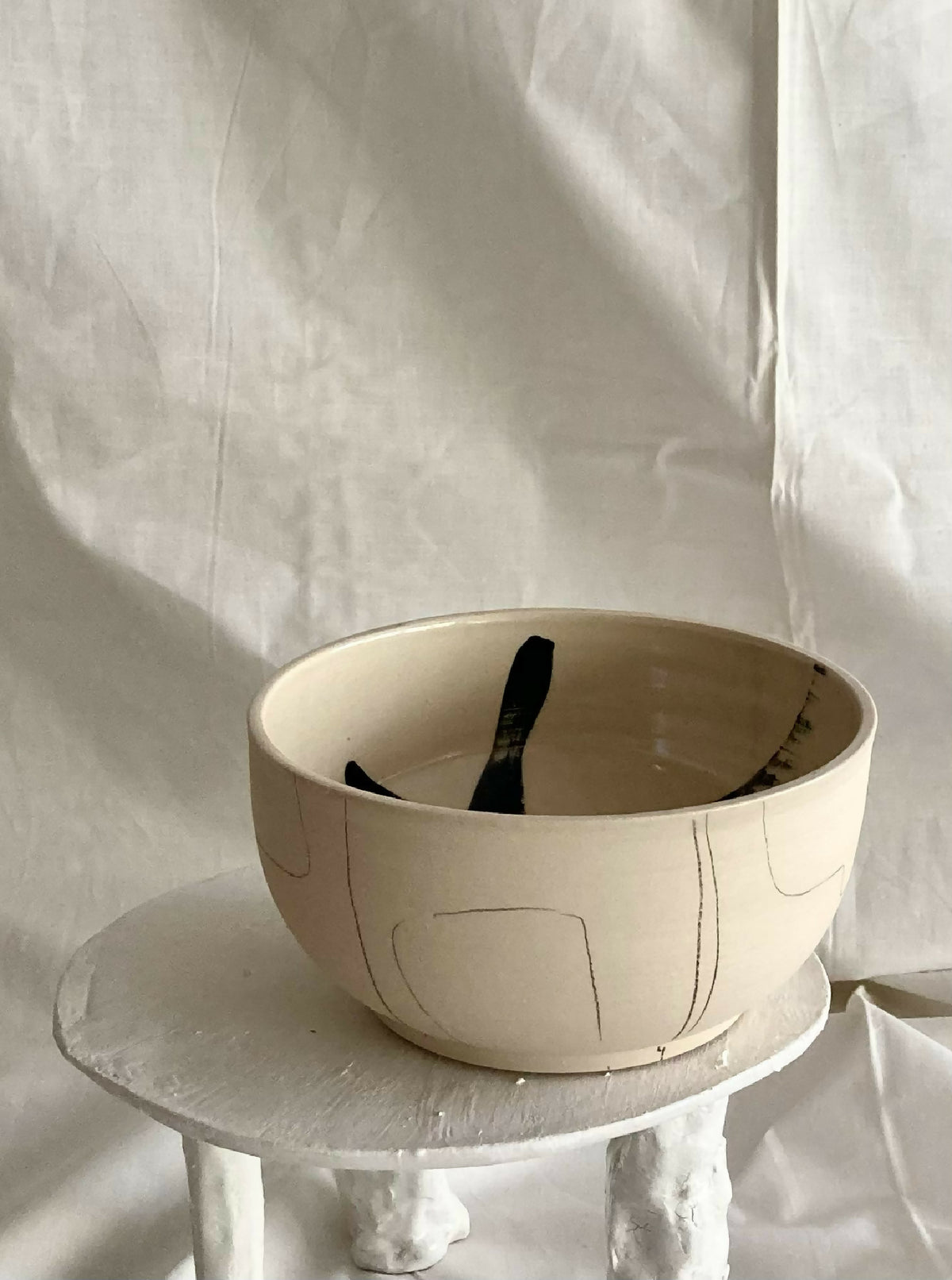 Bol beige avec lignes et motif abstrait noir sur l’extérieur, bords lisses.