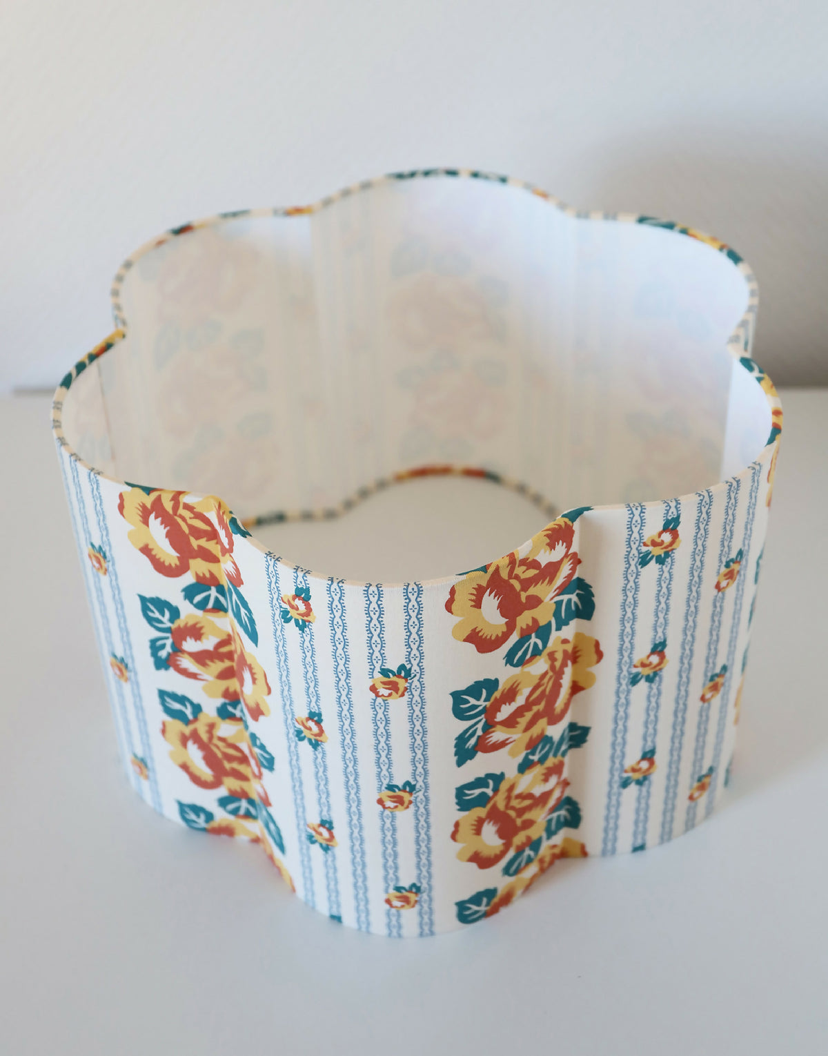 Abat-jour forme fleur en tissu bleu clair, motif floral orange, bord ondulé.
