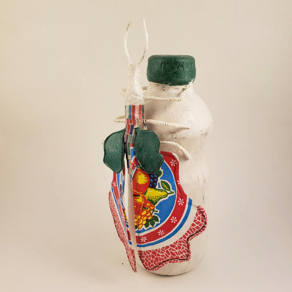 Sculpture posée sur une bouteille, buste blanc, capuchon vert, devant imprimé rouge et bleu