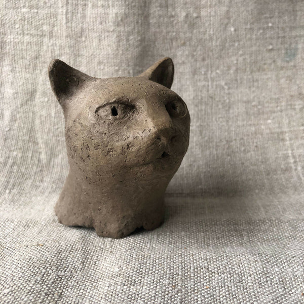 Petite sculpture en argile d’un chat, tête de face, yeux sculptés.