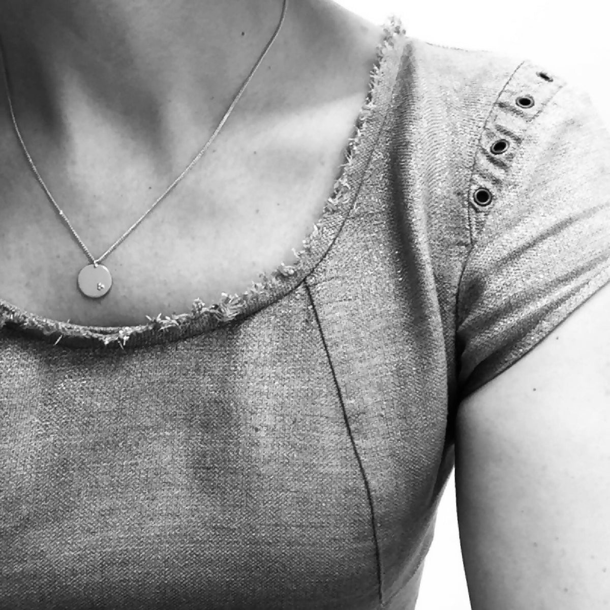 Collier à chaîne fine dorée et pendentif rond clair, près du décolleté