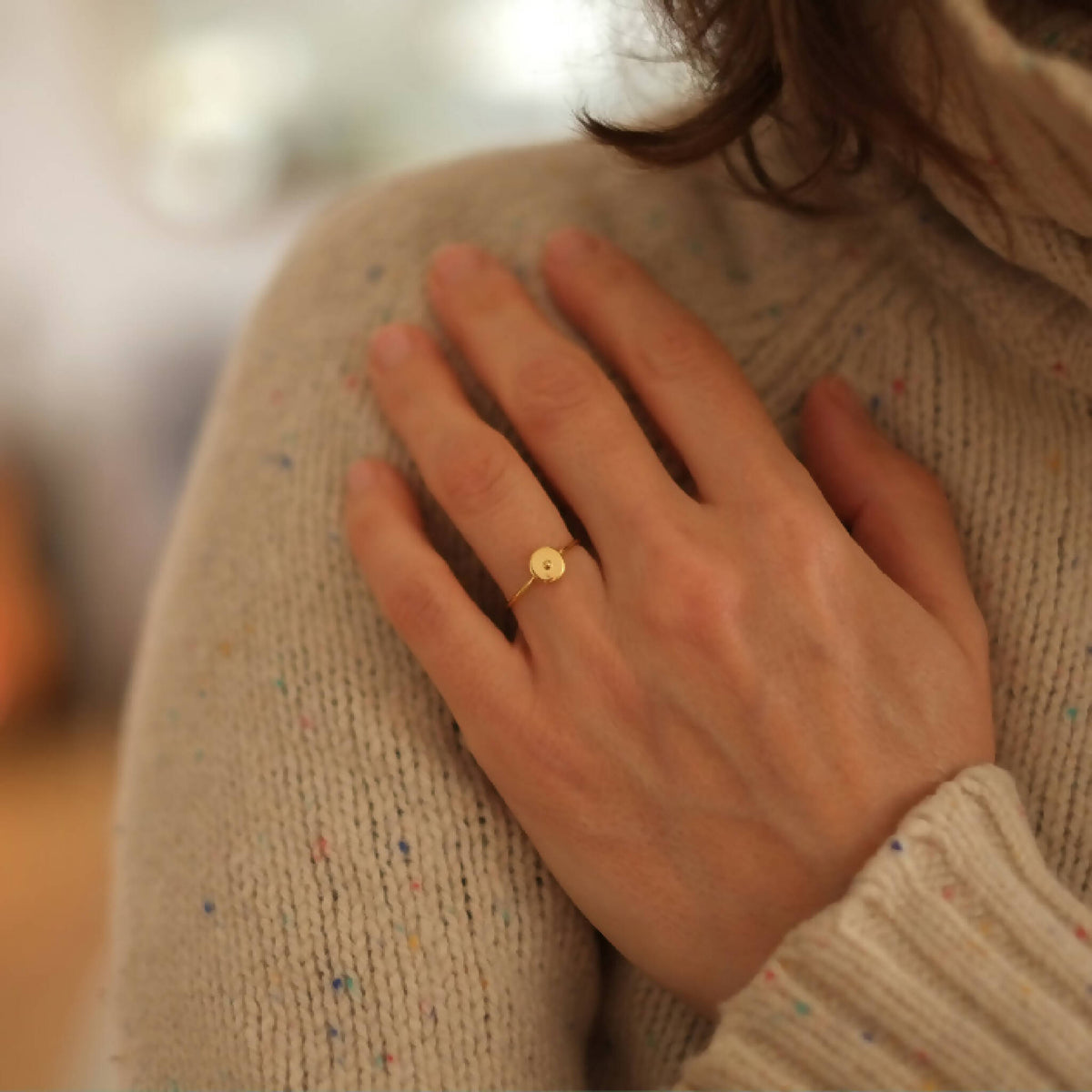 Bague fine dorée avec pastille ronde verte sur le doigt