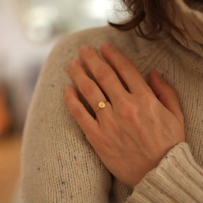 Bague fine dorée avec pastille ronde verte sur le doigt