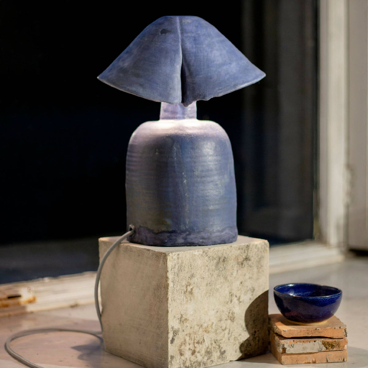 Lampe à double abat-jour bleu sur base en béton, câble noir visible.
