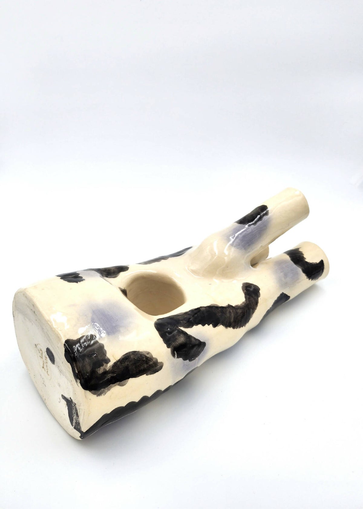 Vase en céramique crème couché avec motifs noirs abstraits et deux ouvertures ovales.