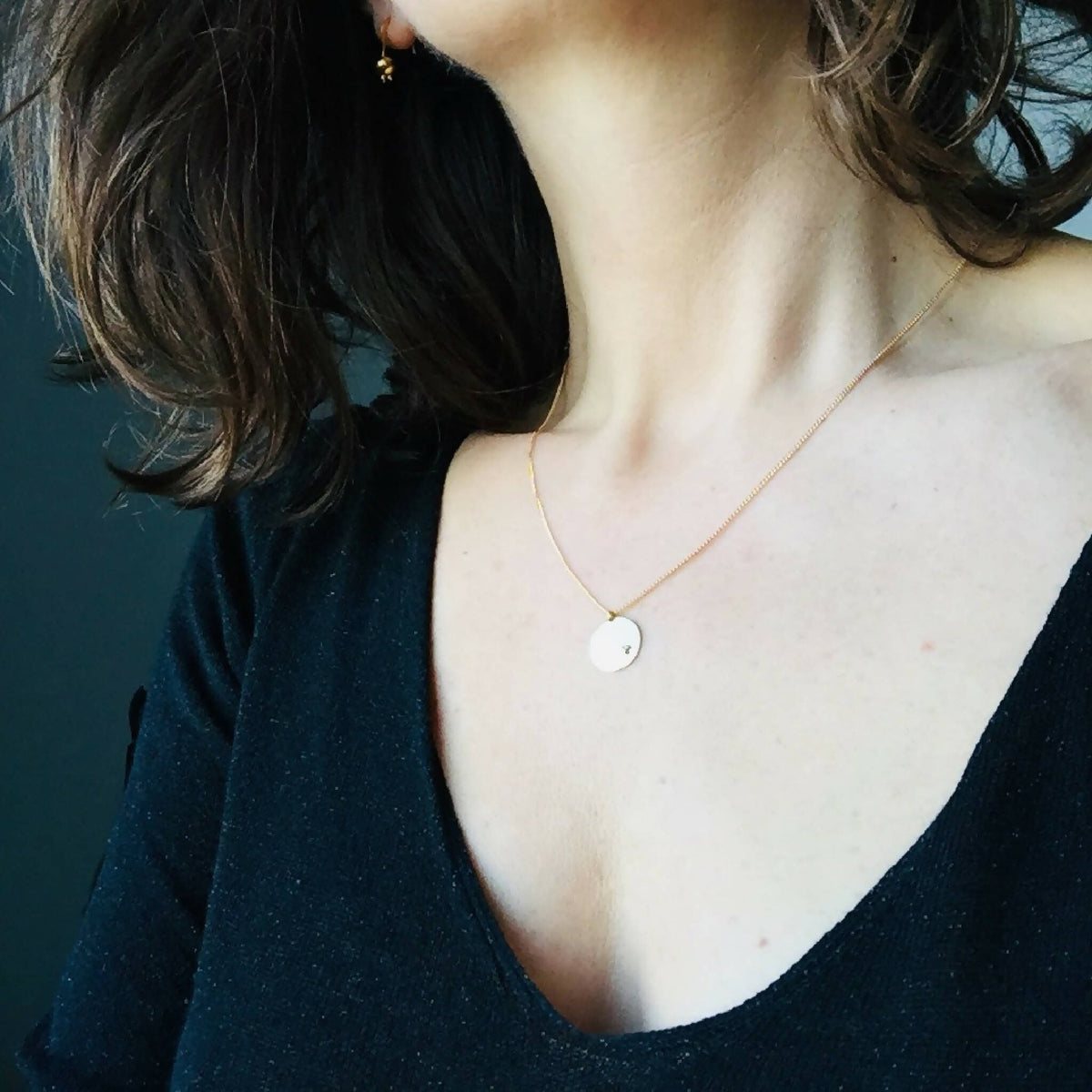 Collier chaîne dorée et pendentif rond clair, porté près du cou