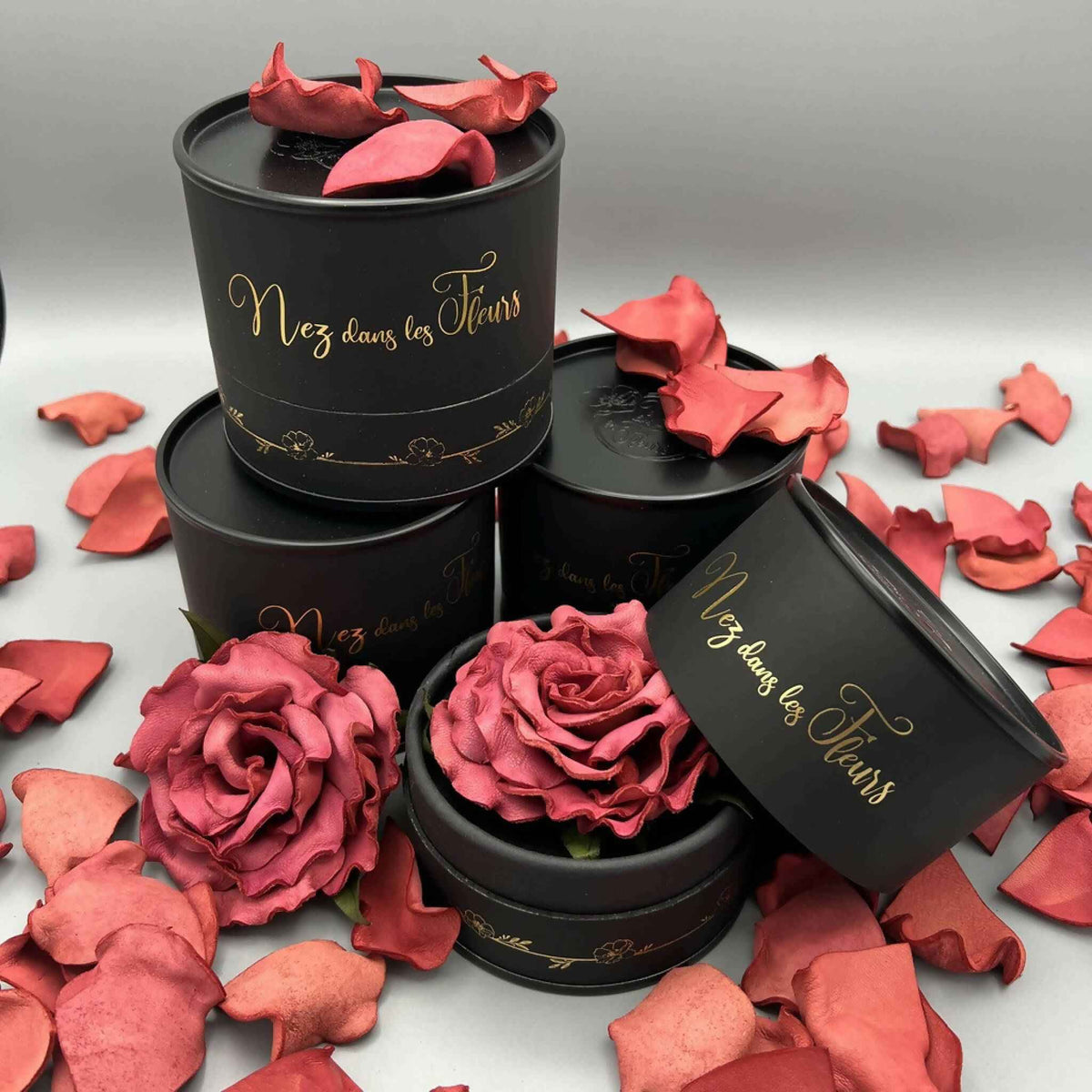 Boîtes parfumées noires avec roses rose ouvertes, pétales rouges autour