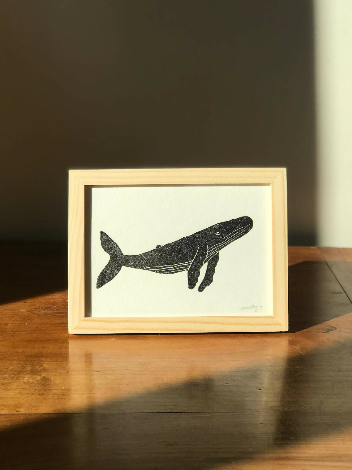 Cadre photo en bois clair avec silhouette de baleine noire, illustration sur fond clair