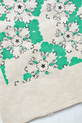 Papier décoratif vert et blanc, motifs floraux et volutes en gros plan.