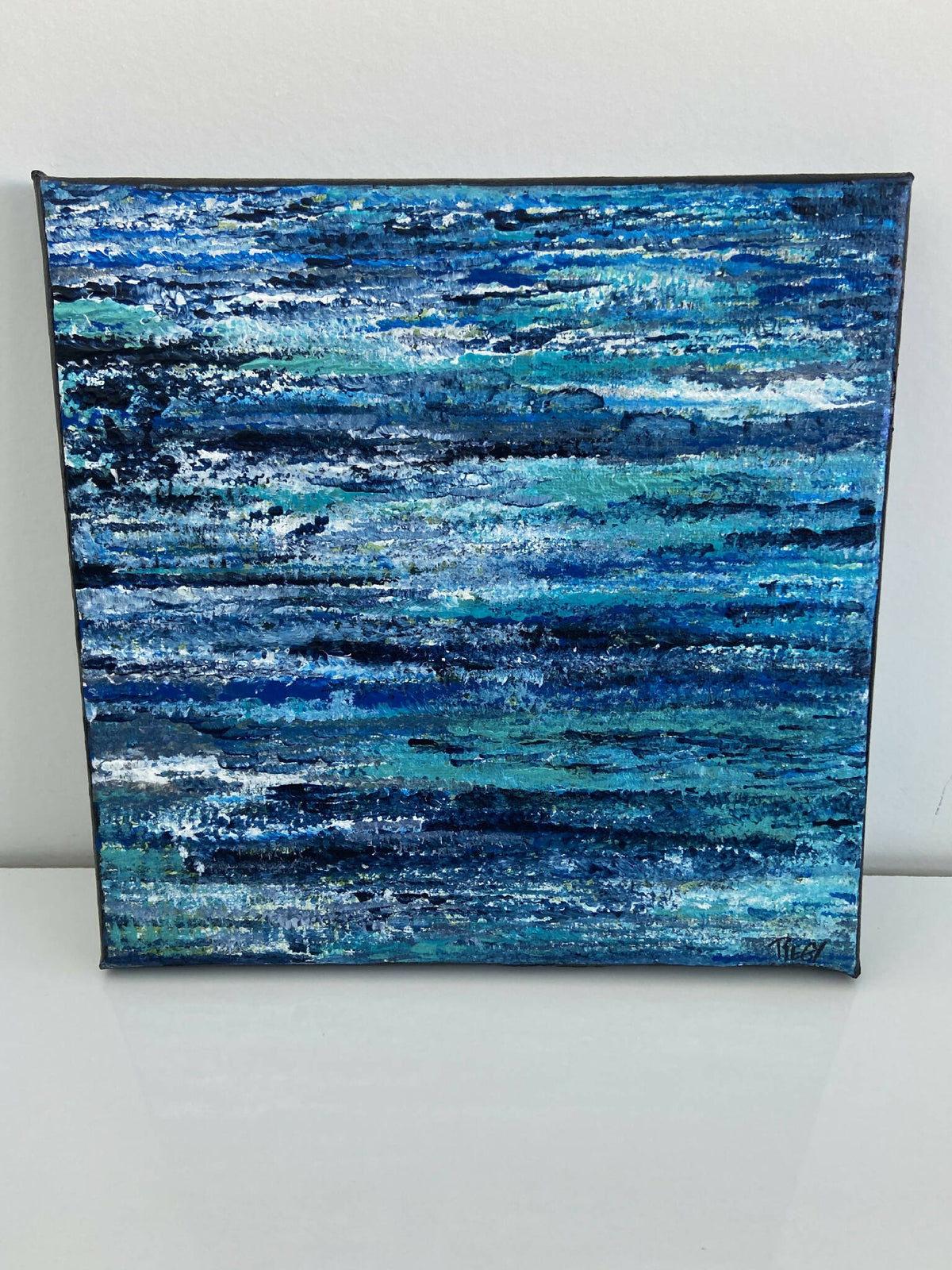 Tableau sur toile carrée, fond bleu avec rubans turquoise et éclats blancs.