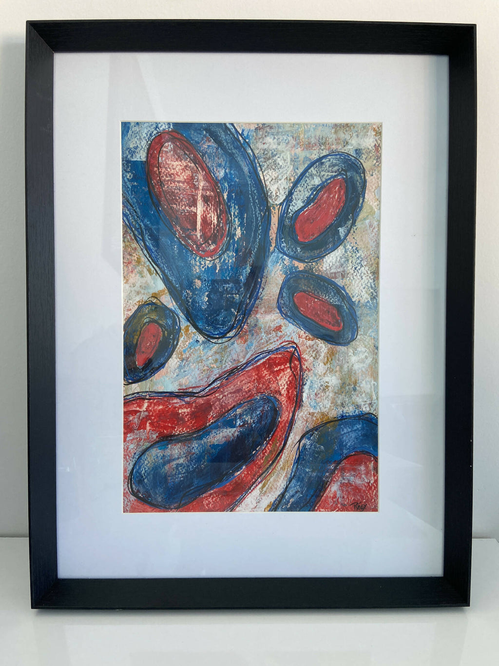 Tableau abstrait encadré, formes ovales bleues et rouges sur fond clair.